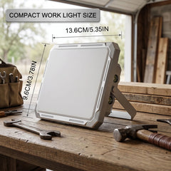 Compact portable LED work light with white housing and fold-out stand, shown on a workbench