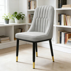 Light gray upholstered dining chair with padded seat, vertical tufted back, gold-tipped legs