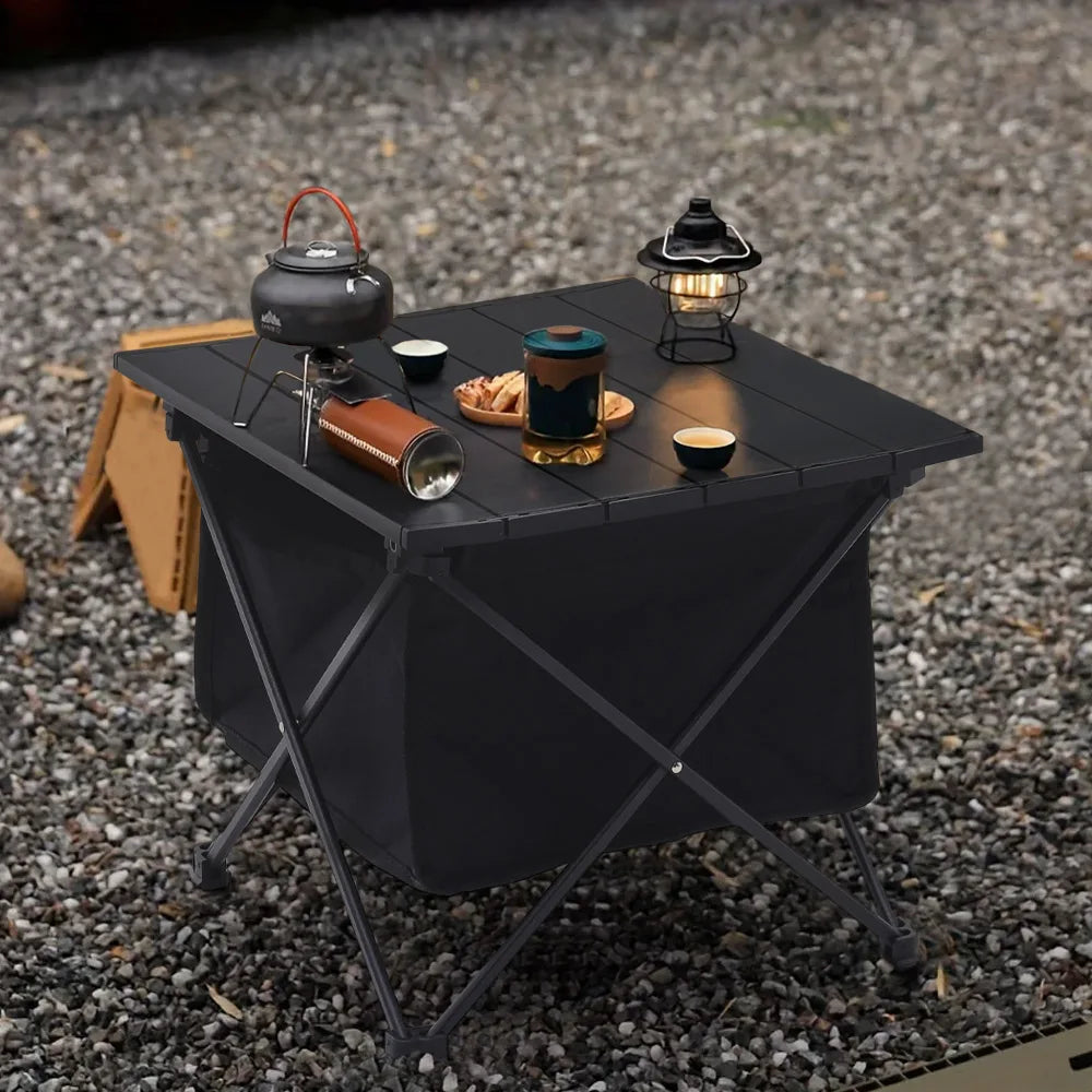 Black camping folding table with slatted top and storage bin, set with cookware