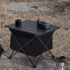 Black portable folding table with slatted top, storage bin front, and compact carry case