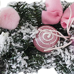 Close-up: frosted pine wreath with pink pom poms and spiral swirl ornament.