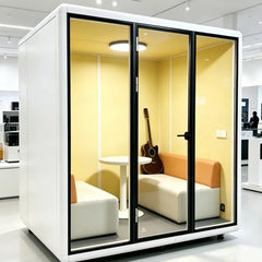 Portable quiet work pod with white frame and glass doors, showing seating and guitar inside