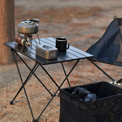 Black portable folding table with slatted surface and storage pouch, with side lantern