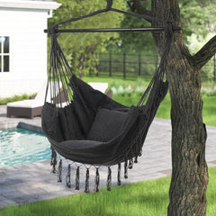 Dark gray canvas hanging swing chair with long fringe tassels and rope straps.