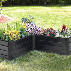 Charcoal black L-shaped metal raised garden bed with layered sides, filled with flowers