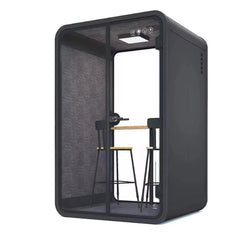 Portable recording pod in dark gray with open glass front, showing chairs and equipment