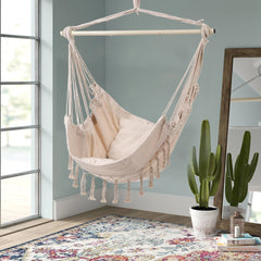 White canvas hanging swing chair with fringe tassels and rope support frame.